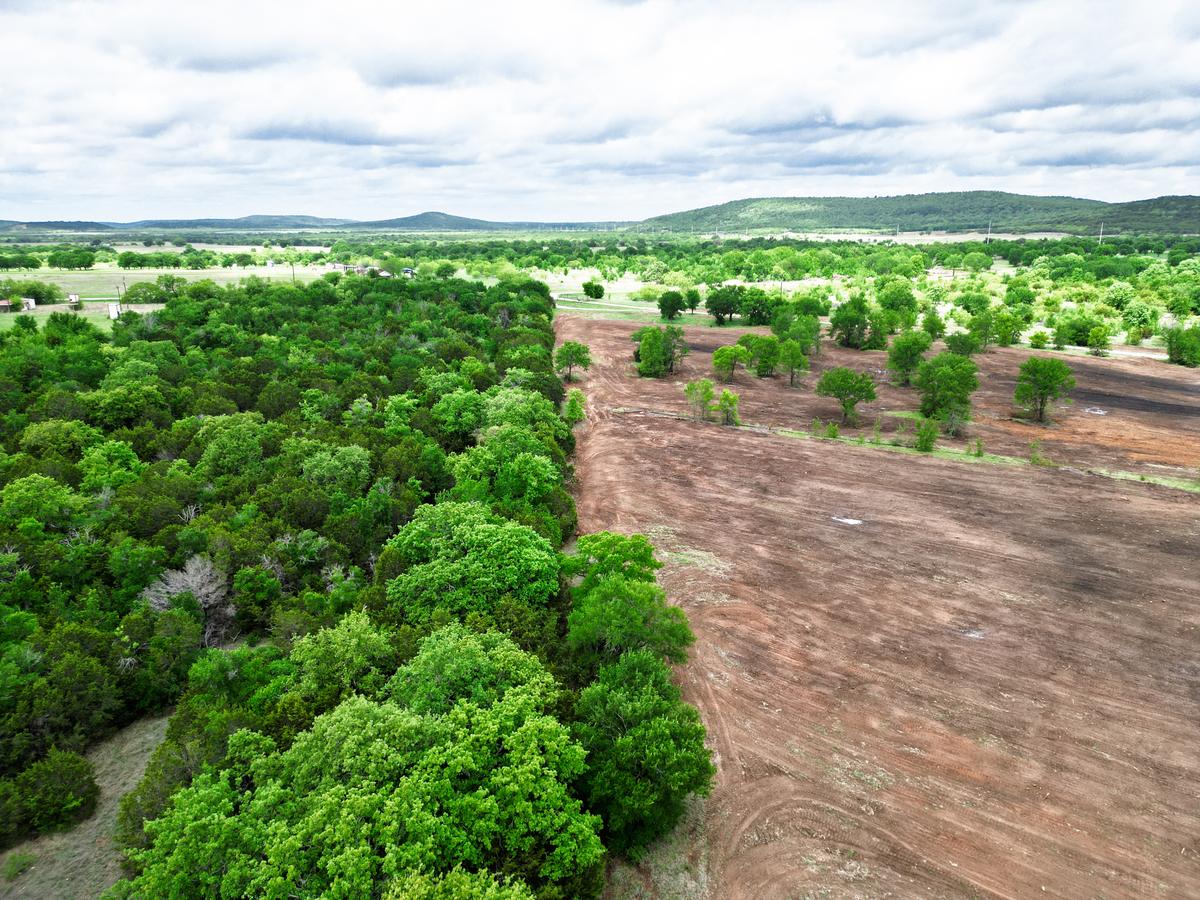 Aerial view of a property where dense green woods stop at a straight edge against a wide field of freshly cleared and raked red dirt