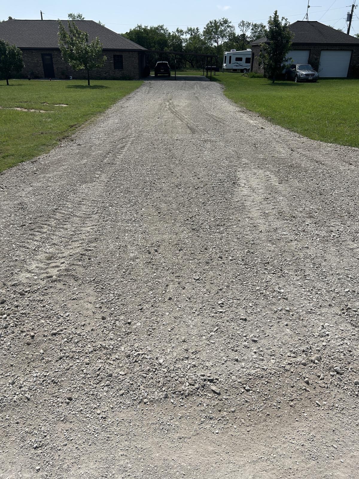 A long, freshly rocked gravel driveway running between two brick houses in Jacksboro, Texas, crowned in the middle and mown grass on both sides