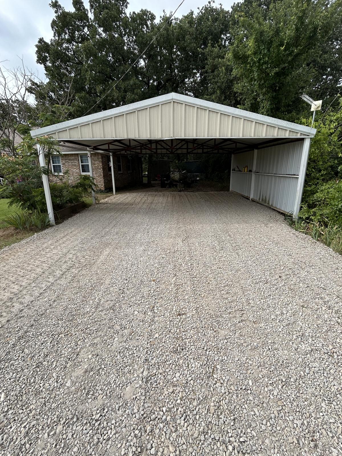 A gravel driveway in Perrin, Texas freshly rocked from the road up and through an open carport beside a brick house