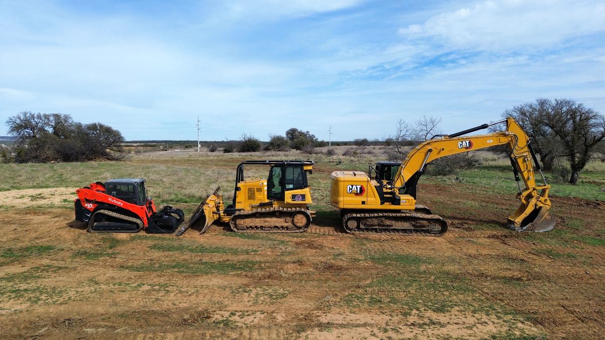 A Kubota track loader, a Cat dozer and a Cat 320 excavator lined up side by side in a pasture