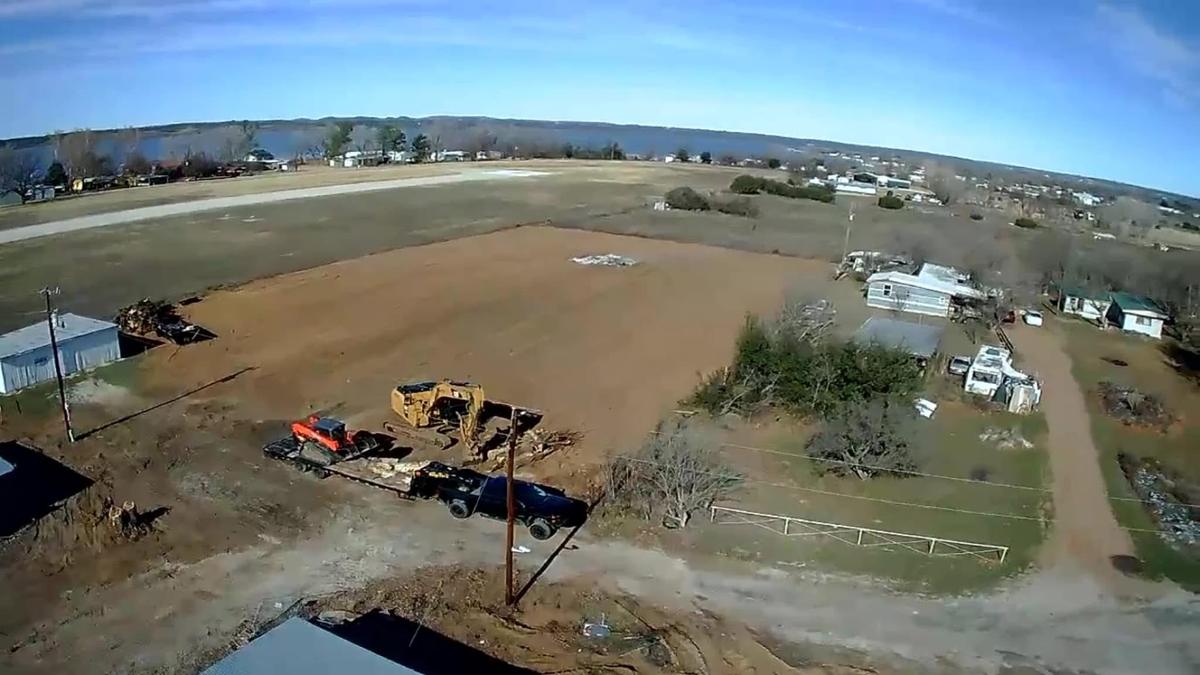 Aerial view of a cleared and leveled lot near a lake, with an excavator and a skid steer loaded on a lowboy trailer at the edge