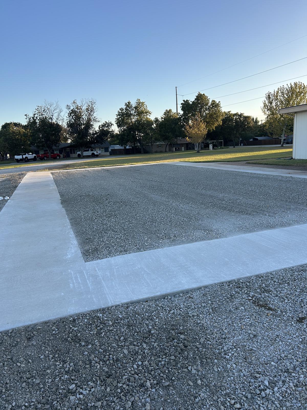 A compacted gravel building pad in Graham, Texas, framed by new concrete aprons with a poured approach running out to the street