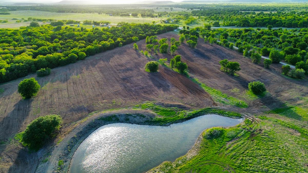 The same stock tank in summer, dug out and full of water with reshaped banks, the surrounding flat cleared to bare worked ground